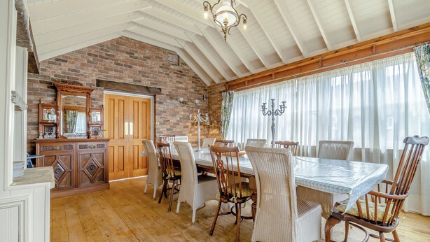 Un comedor con pared de ladrillo, techo de madera y una mesa grande con sillas.