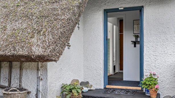 Ein rustikales Cottage mit Strohdach, einer Holztür und einer kleinen Veranda mit Blumentöpfen.