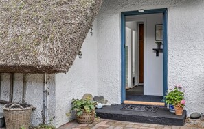 Ein rustikales Cottage mit Strohdach, einer Holztür und einer kleinen Veranda mit Blumentöpfen.