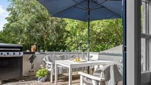 Eine Außenpatio mit Grill, Tisch, Stühlen und einem großen Sonnenschirm.
