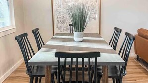 A dining area with a wooden table, six chairs, a hanging light fixture, and a framed map on the wall. - Paddlewhack Cabin 2 - FlyBridge (Jefferson)