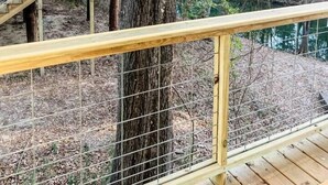 A wooden deck with a metal railing overlooking a natural landscape with trees and a small building. - Paddlewhack Cabin 3-The Keel/Pet Friendly (Jefferson)
