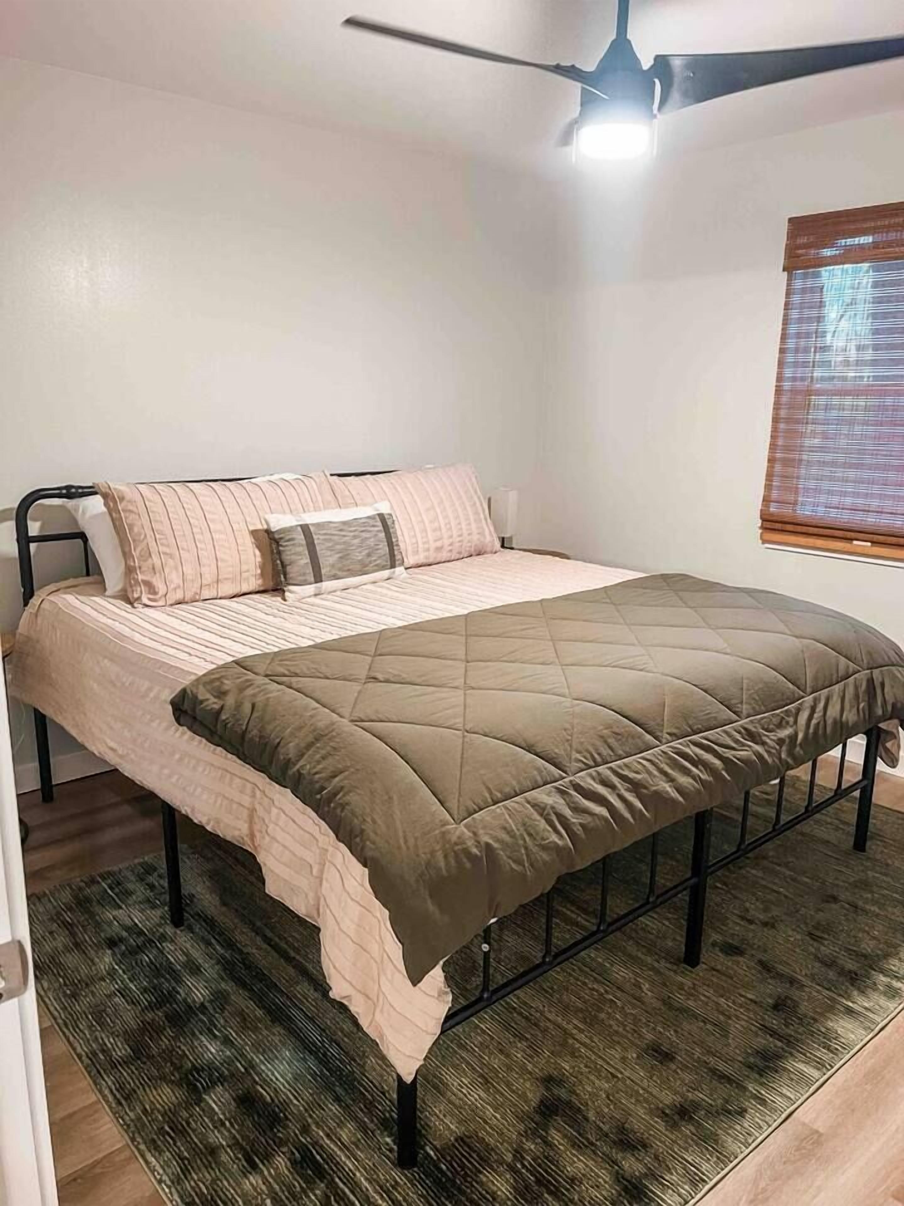 Una cama individual con cabecera acolchada, una mesita de noche y un ventilador de techo.