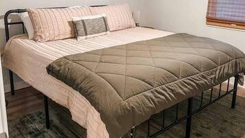 Una cama individual con cabecera acolchada, una mesita de noche y un ventilador de techo.