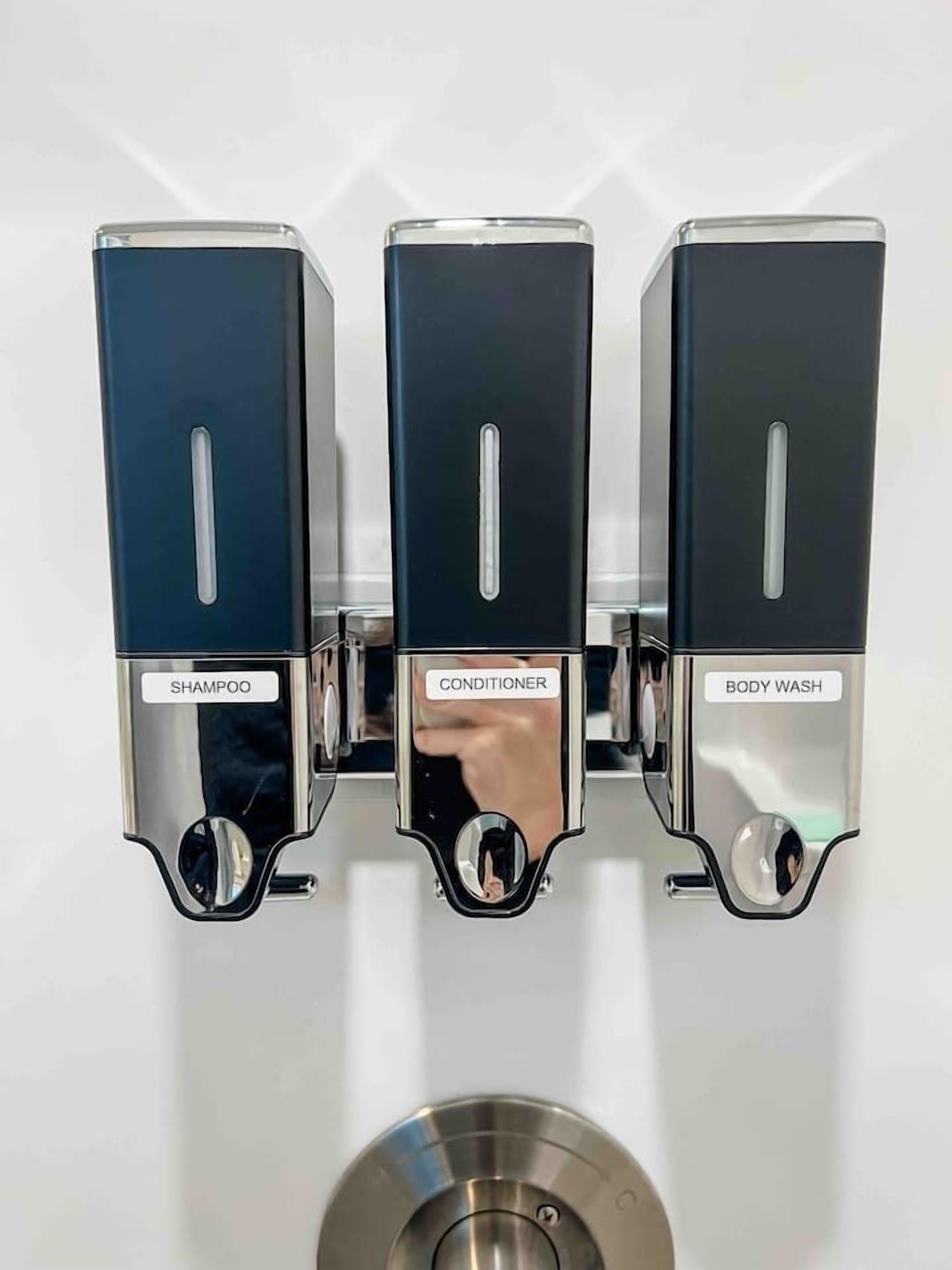 Een wandbevestigd doseerapparaat met drie vakken, gelabeld 'SHAMPOO', 'CONDITIONER' en 'BODY WASH'.