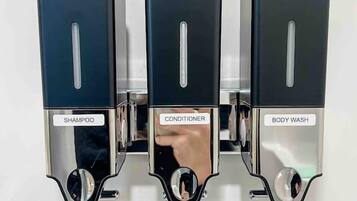 Een wandbevestigd doseerapparaat met drie vakken, gelabeld 'SHAMPOO', 'CONDITIONER' en 'BODY WASH'.