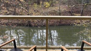 A wooden deck with two chairs and a small table, overlooking a calm river and forested area. - Paddlewhack Cabin 5-The Bow (Jefferson)