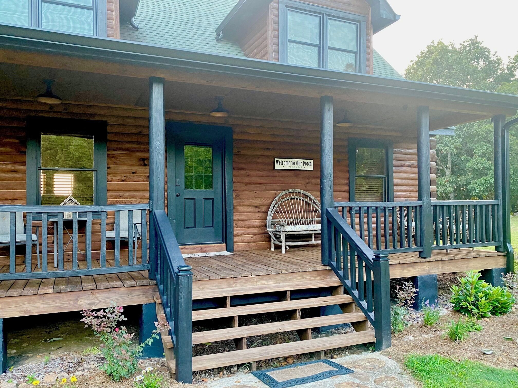A wooden cabin with a porch, a welcome sign, and a bench.