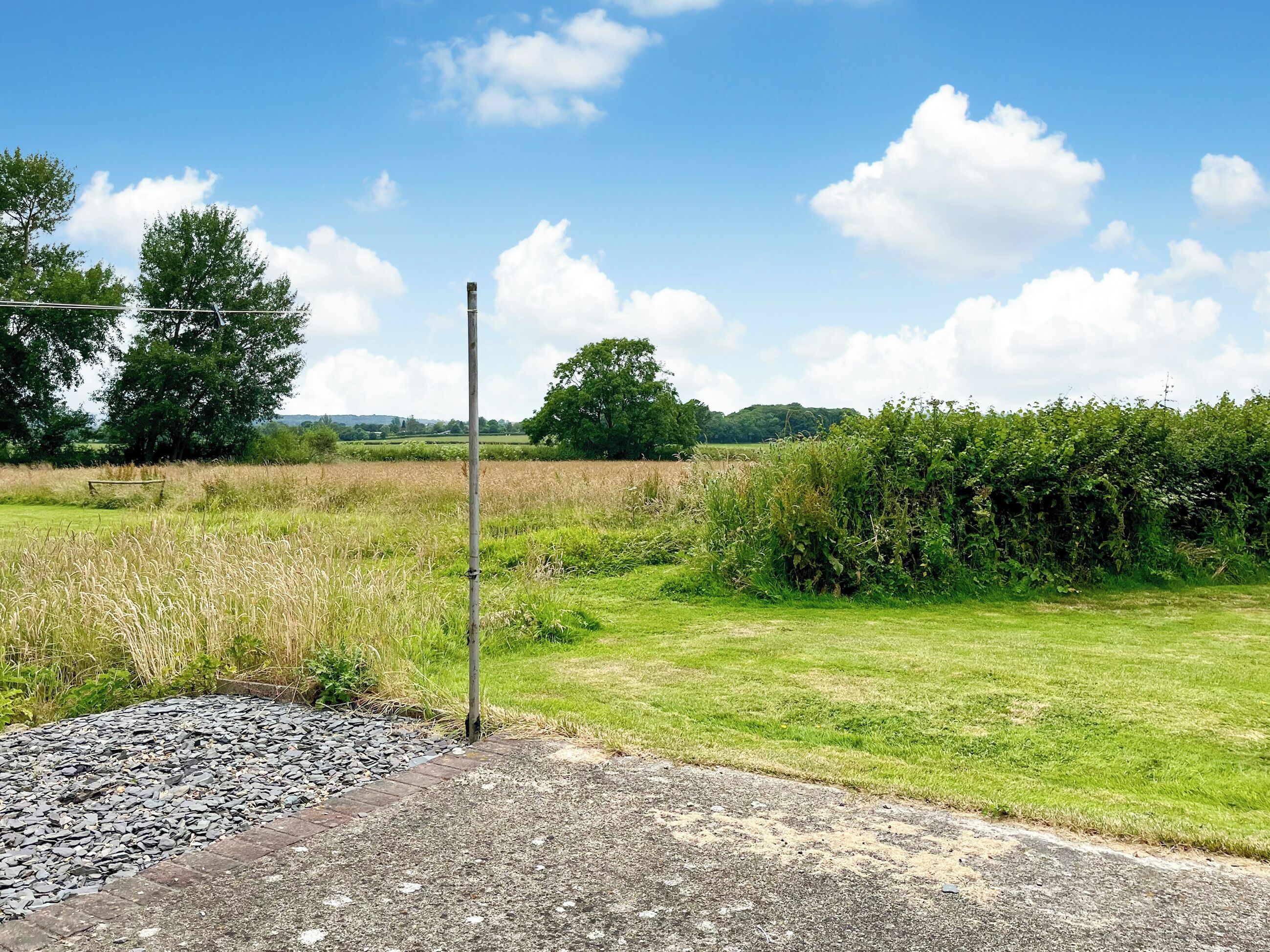 A rural landscape with a gravel path, grassy fields, and a metal pole.