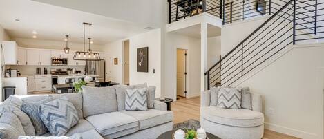 A modern living room with a sectional sofa, a round coffee table, and a staircase with a black railing.