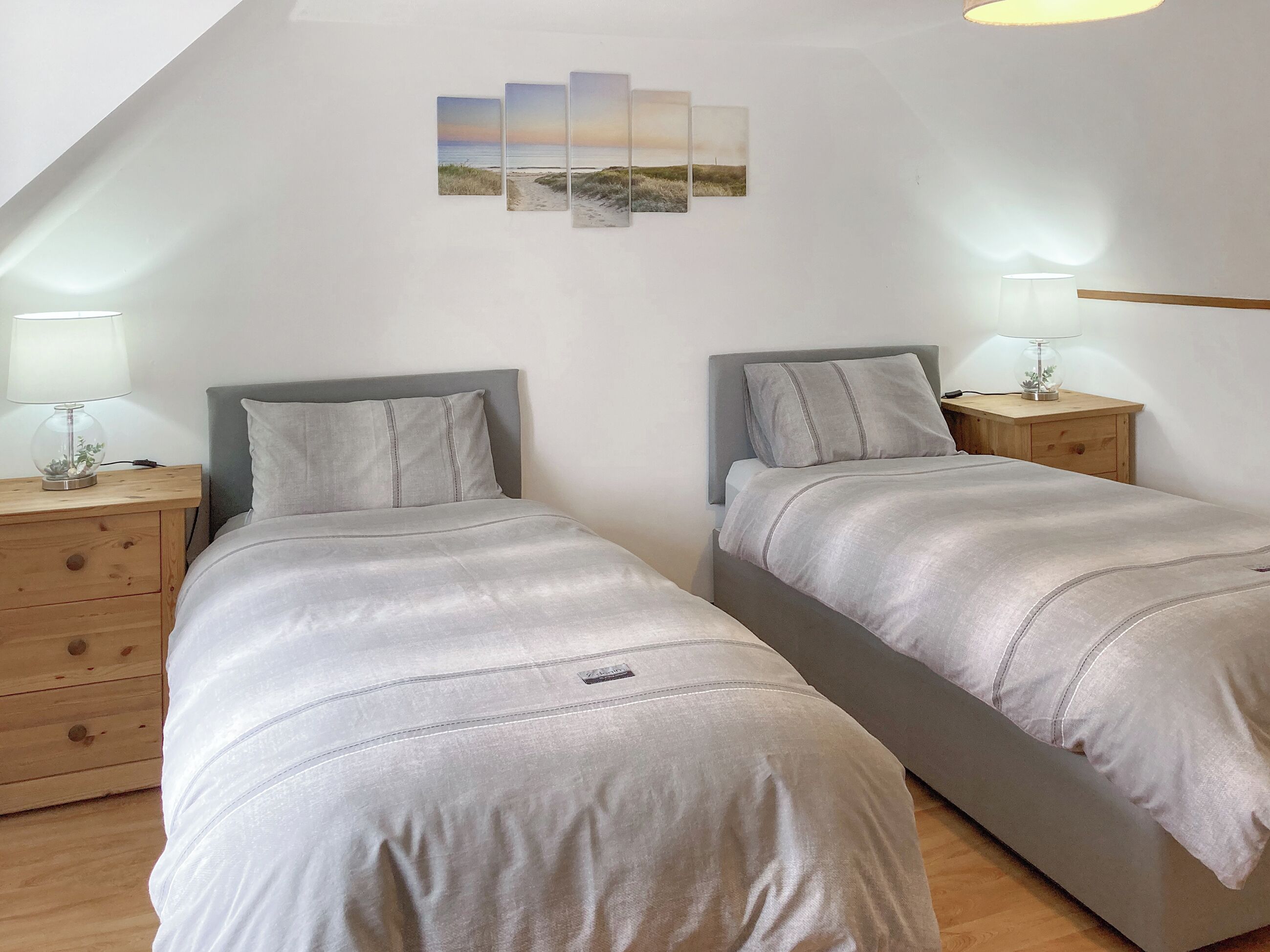 A bedroom with two beds, a wooden nightstand with a lamp, and a wall-mounted lamp.