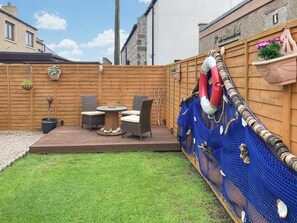 A patio area with a round table and two chairs, surrounded by a wooden fence and a blue netting structure.