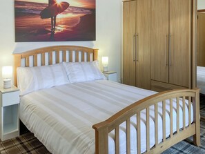 A neatly made bed with striped bedding, wooden headboard, bedside lamps, and a wooden wardrobe with two doors.