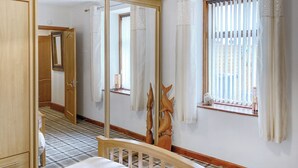 Una habitación de hotel con cama, espejo, ventana con cortinas y cabecera de madera.