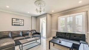 A living room with two black leather sofas, a coffee table, a chandelier, and a framed picture on the wall. - Pet-Friendly Valley Stream Duplex - 1 Mi to Mall! (Valley Stream)