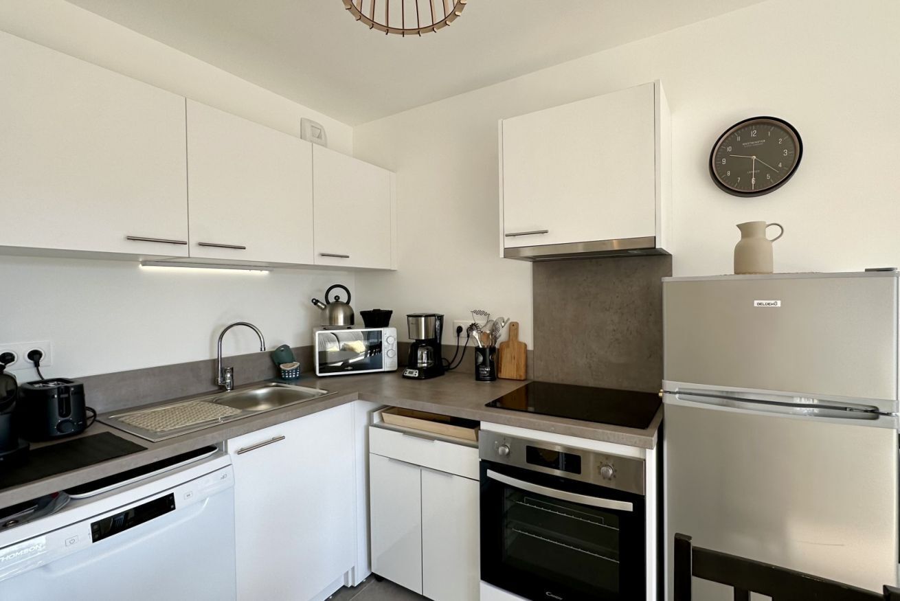 Una cocina moderna con gabinetes blancos, un refrigerador de acero inoxidable, un microondas, un tostador y un fregadero.