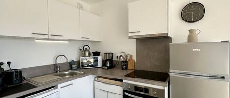 Una cocina moderna con gabinetes blancos, un refrigerador de acero inoxidable, un microondas, un tostador y un fregadero.