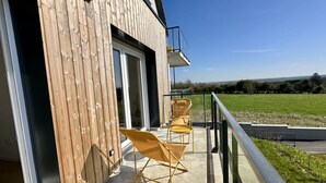 Ein Balkon mit zwei Klappstühlen, einer Holzwand und Blick auf ein grünes Feld.