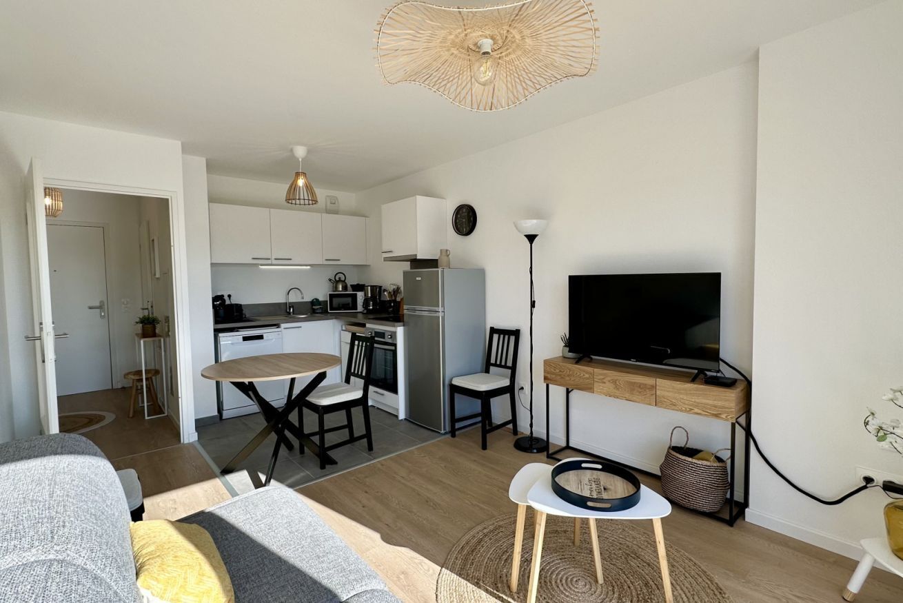 A compact living space with a kitchenette, dining area, and a TV mounted on a wooden cabinet.