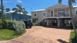 A two-story house with a covered porch and a brick driveway. - Cozy keys getaway  (Ramrod Key)