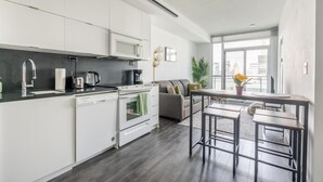 A modern kitchen with white cabinets, a built-in oven, and a dining area with a table and bar stools.
