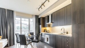 A modern kitchen with dark wood cabinets, stainless steel appliances, and a dining area with a glass table and black chairs. - GLOBALSTAY. Stylish 1 Bedroom in Downtown Toronto (Toronto/Canada)