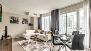 A modern living room with a white sofa, a glass dining table, and a view of the city through large windows. - GLOBALSTAY. Stylish 1 Bedroom in Downtown Toronto (Toronto/Canada)