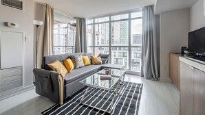 Un salon moderne avec un canapé, une table basse en verre et une vue sur la ville grâce à de grandes fenêtres.