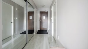 Un couloir avec une porte en verre, une porte en bois et un paillasson noir à l’entrée.