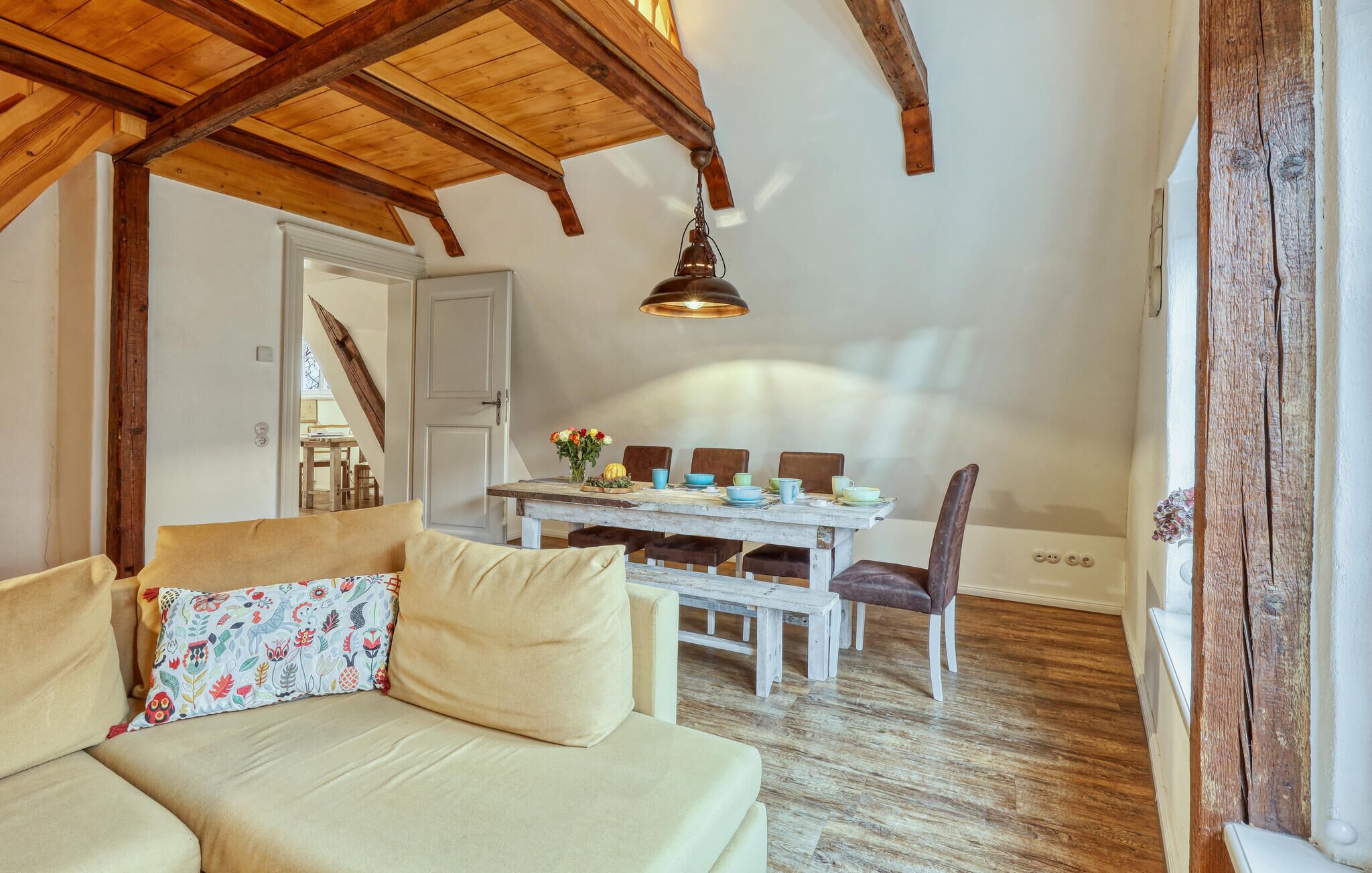 Un acogedor espacio tipo loft con techo de madera, una mesa de comedor decorada con vajilla colorida y un sofá con cojines estampados.