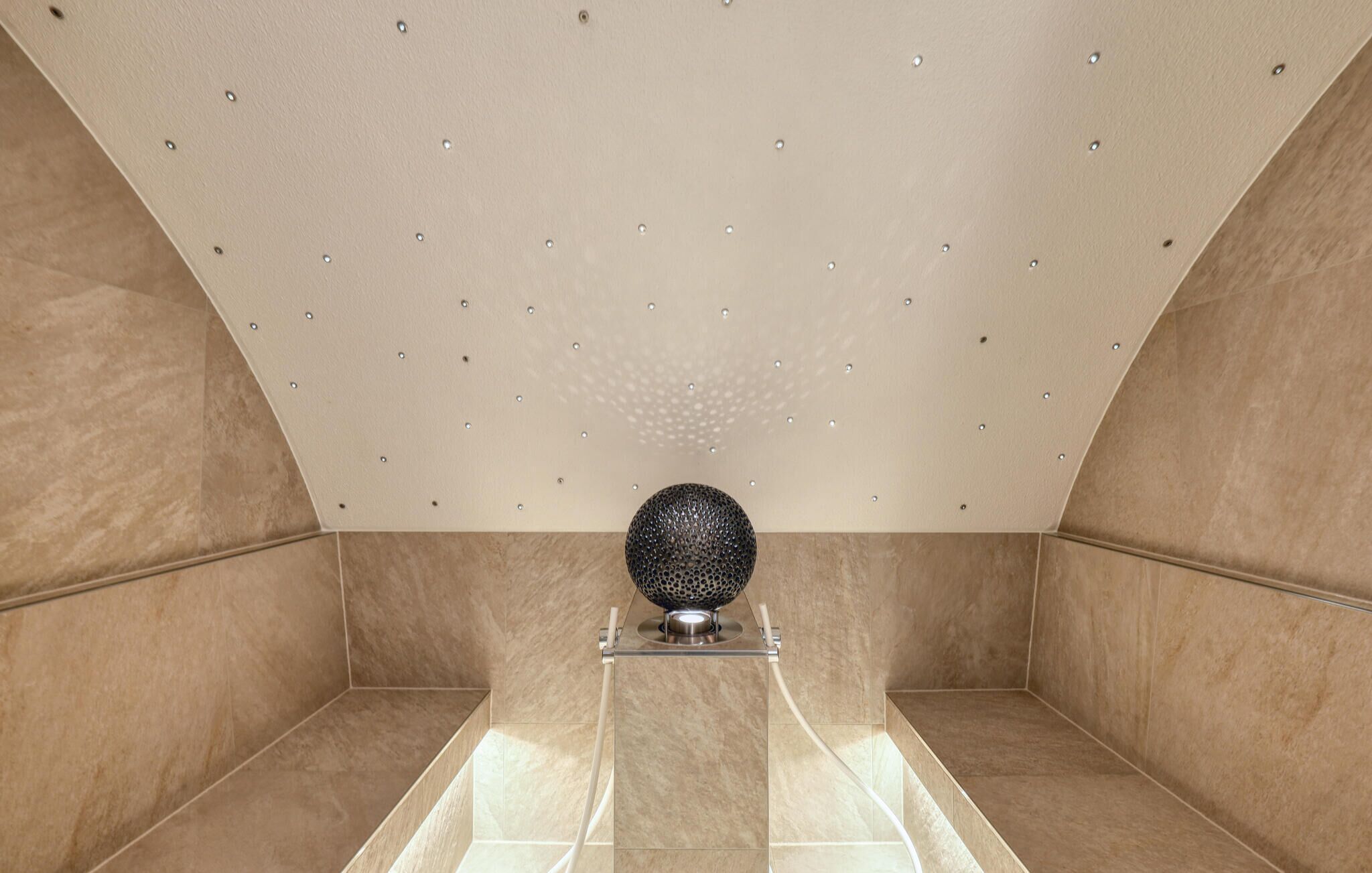 Un baño moderno con un diseño geométrico en el techo, un objeto esférico central sobre un pedestal y suelo de baldosas.