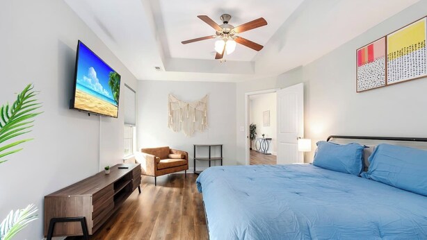 Una camera da letto moderna con un letto grande, un ventilatore a soffitto, un televisore a parete e un pavimento in legno.