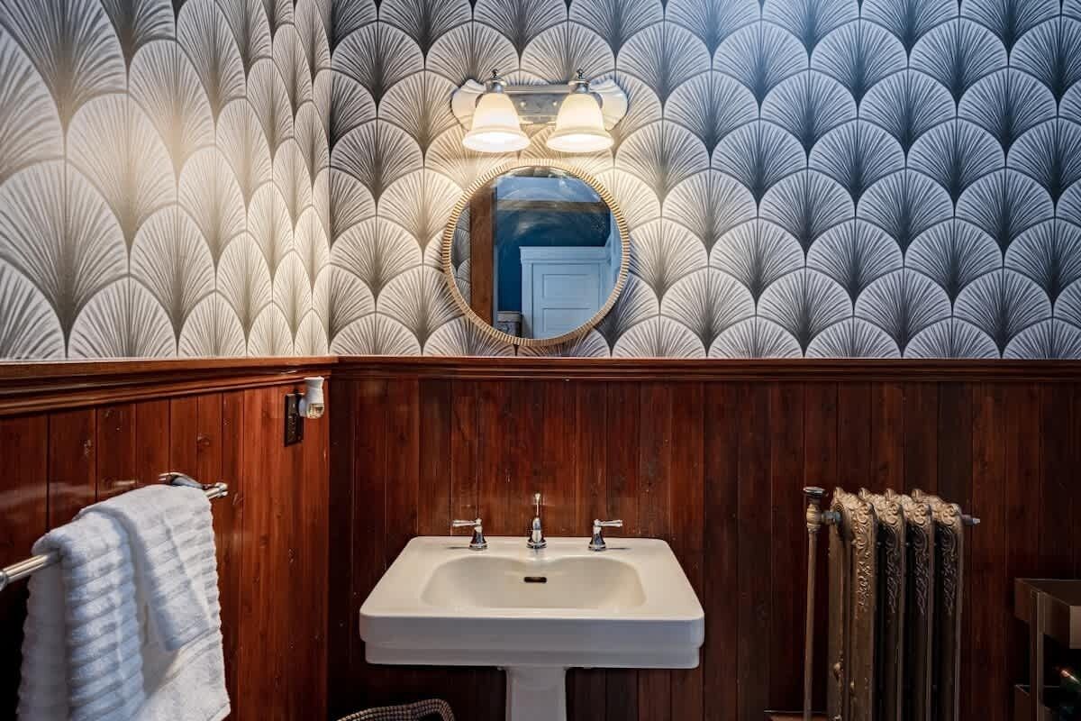 A bathroom with a wooden vanity, a white sink, and a patterned wallpaper.