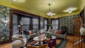 Un salon avec un papier peint à motifs, un ensemble de canapés à carreaux, une table basse ronde et un lustre.