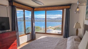 Ein Schlafzimmer mit einem großen Bett, einem Fernseher, einer Lampe und Meerblick.