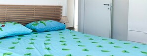 A bed with a blue sheet and green leaf pattern, two pillows, a wooden headboard, a lamp, and a white wardrobe.