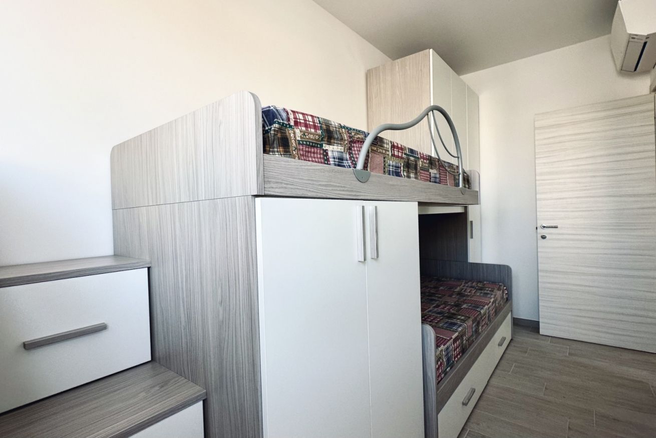 Una cama litera con escritorio y cajones, una colcha estampada y una puerta cerrada.
