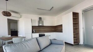 Una sala de estar moderna con un sofá gris, una mesa de comedor y una zona de cocina con armarios blancos y encimera de madera.