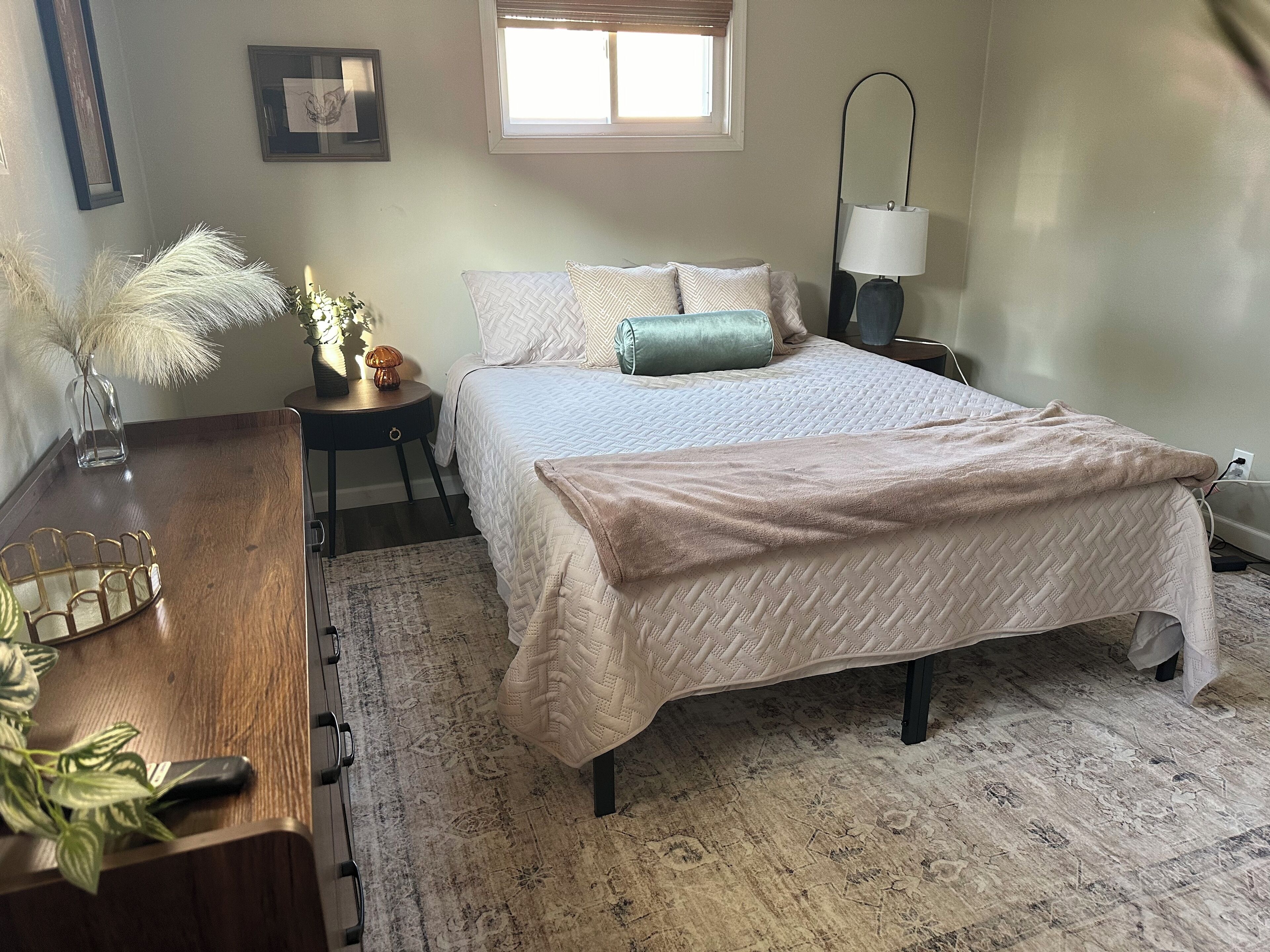 Quarto bem arrumado com cama, mesa de cabeceira, abajur e uma janela.