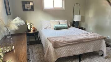 Quarto bem arrumado com cama, mesa de cabeceira, abajur e uma janela.