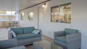 Un espace de vie extérieur moderne, comprenant un canapé et des fauteuils, une porte vitrée et une vue sur l’immeuble voisin.