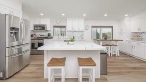 Une cuisine moderne avec des meubles blancs, des appareils en acier inoxydable et un îlot central doté de tabourets.