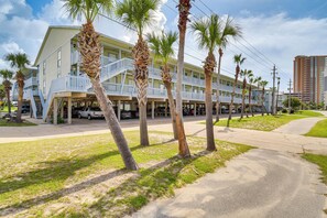 A beachfront hotel with multiple balconies, palm trees, and a parking area. - Gulf Shores Condo w/ Pool: Walk to Beaches! (Gulf Shores)