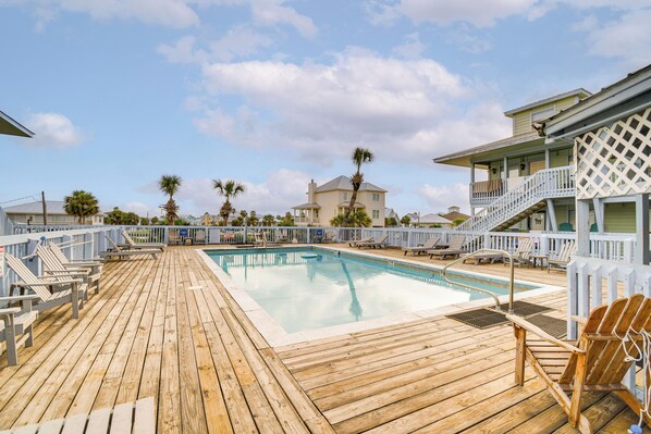 A wooden deck with a pool, lounge chairs, and a building with a balcony. - Gulf Shores Condo w/ Pool: Walk to Beaches! (Gulf Shores)