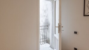 En dörröppning som leder ut till en balkong med ett metallräcke, en vit dörr med ett mässingshandtag och en väggmonterad ljusströmbrytare.