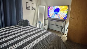 Quarto com uma cama, televisão, escrivaninha e porta.