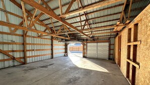 Amplo espaço interior com pé-direito alto e vigas de madeira, apresentando uma porta de garagem e chão de concreto.