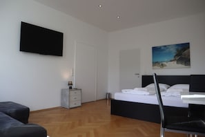 A bedroom with a bed, a flat-screen TV, a painting, a desk, and a chair.