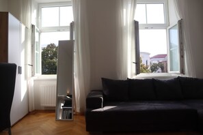 A room with a dark sofa, a radiator, and a window with curtains.