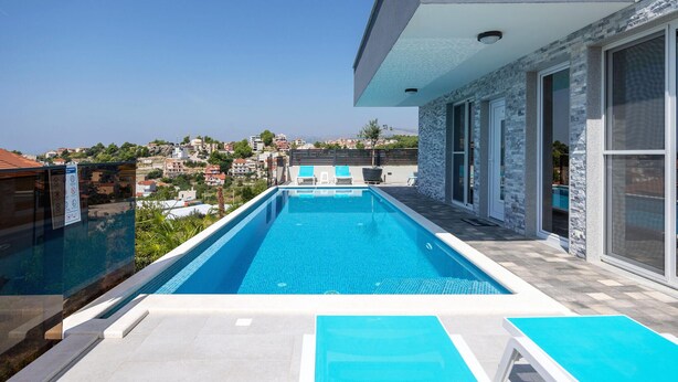 Une piscine extérieure moderne, avec une eau d’un bleu limpide, entourée d’un mur de pierre et dotée de grandes fenêtres.